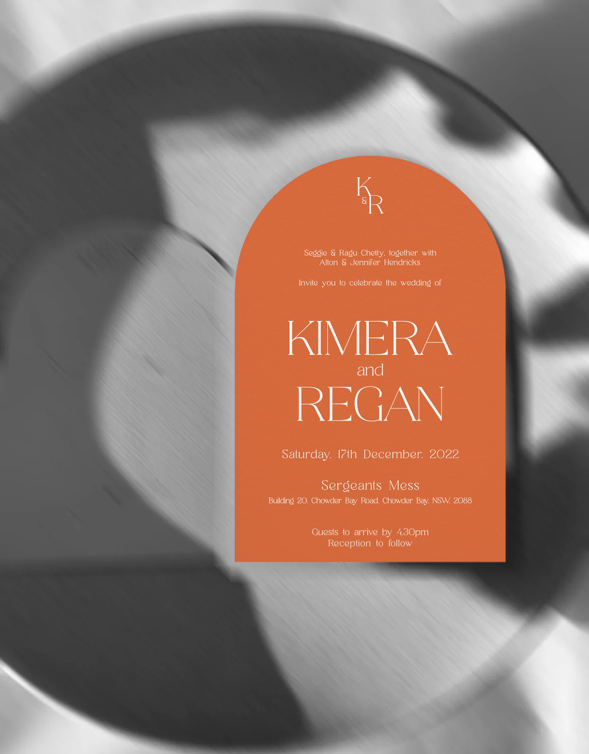 Black and white flatlay image with a burnt orange, arch wedding invitation with white ink on top.