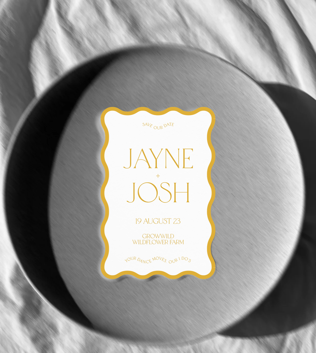 Mockup of a wave shaped save the date with a yellow border and yellow text in front of a black and white image of a plate.