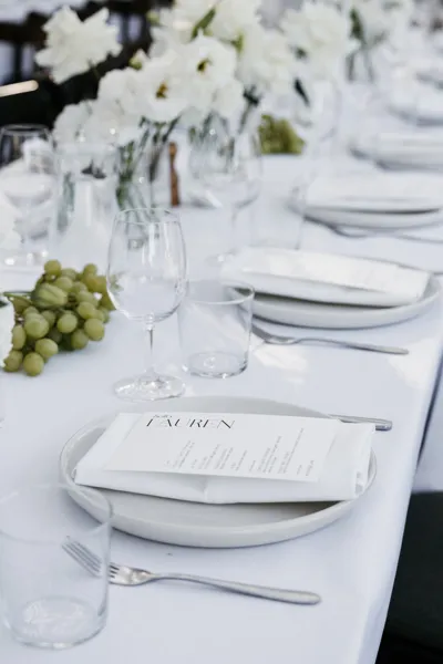 Wedding table setup with white linen and white rectangle dual menu-place cards. White florals are in the background.