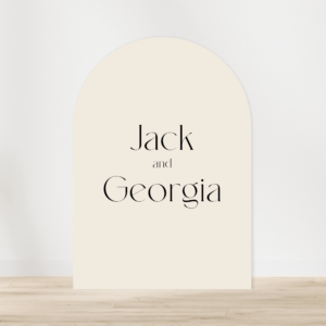 Arch welcome sign from the Evermore collection with black text saying 'Jack and Georgia' leaning against a white wall with timber floorboards.