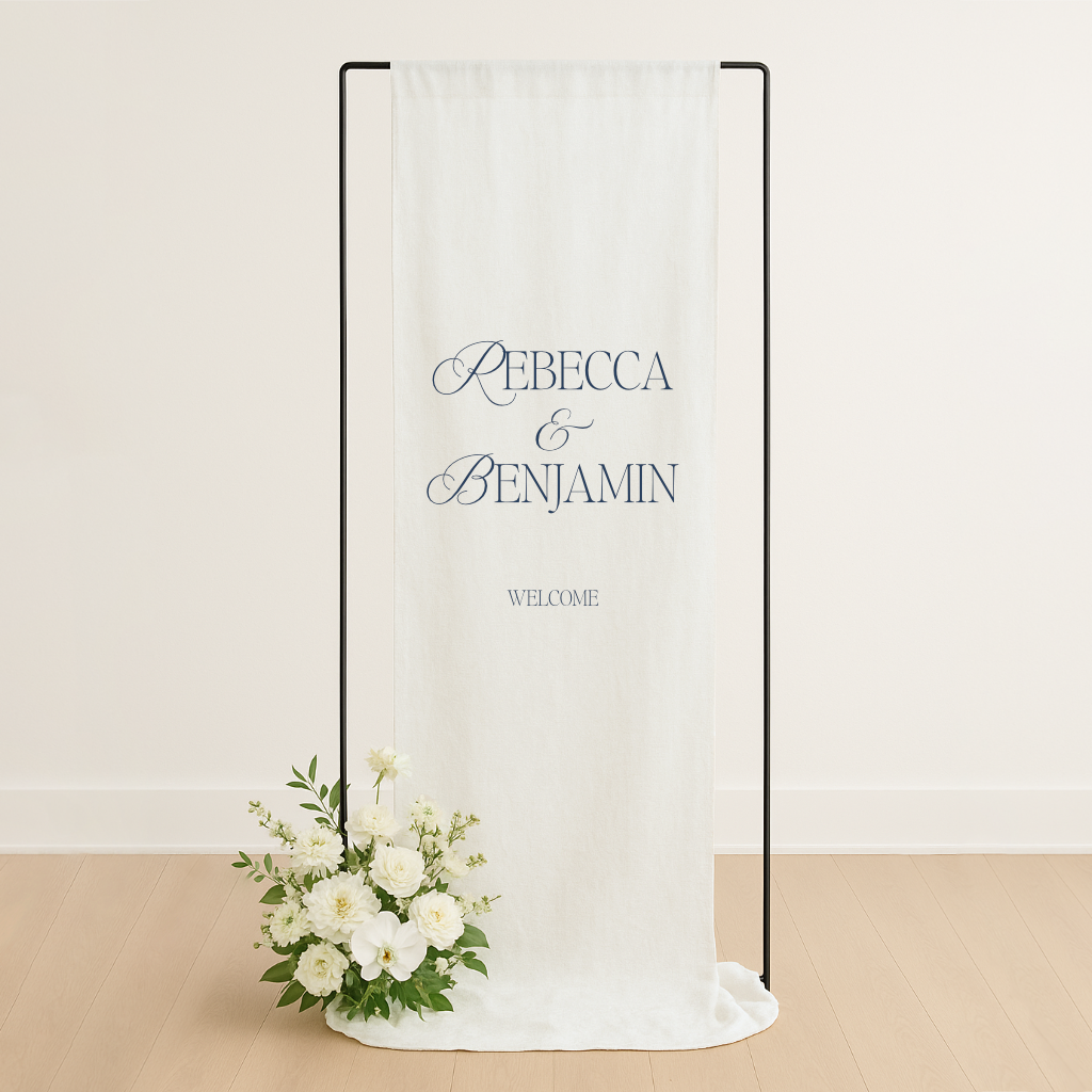 Linen wedding welcome sign hanging on a black metal frame, styled with white roses and greenery at the base – semi-custom signage by Gracie Creative, Australia.