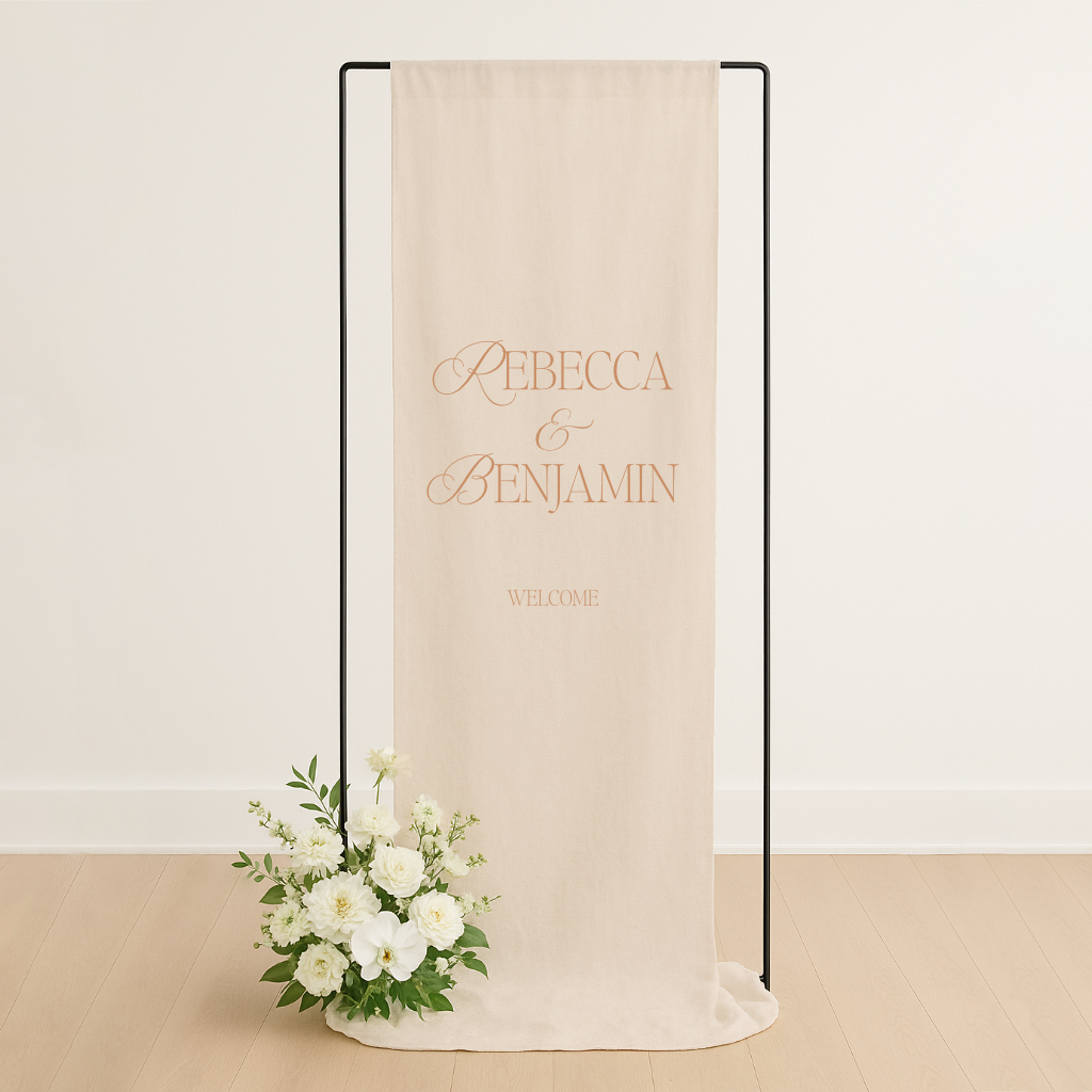 Linen wedding welcome sign hanging on a black metal frame, styled with white roses and greenery at the base – semi-custom signage by Gracie Creative, Australia.