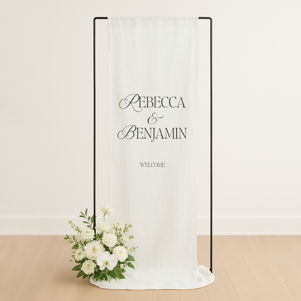 Linen wedding welcome sign hanging on a black metal frame, styled with white roses and greenery at the base – semi-custom signage by Gracie Creative, Australia.