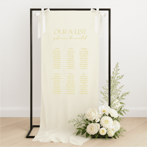 Linen wedding seating chart hanging on a black metal frame with white ribbon, featuring yellow text for with heading 'our a-list', styled with white roses and greenery at the base – semi-custom signage by Gracie Creative, Australia.