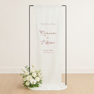 Linen, fabric wedding welcome sign. Semi-custom design hanging from black stand with white flowers at base.