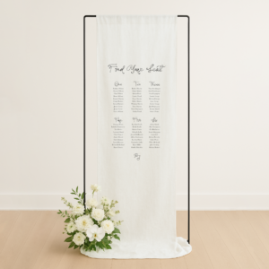 Linen, fabric wedding seating chart. Semi-custom design hanging from black stand with white flowers at base.
